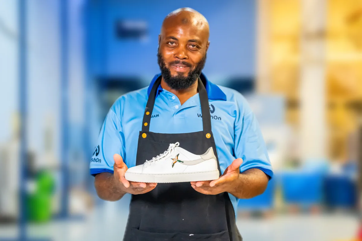 ShoeCare technician in a work apron holding a freshly cleaned white leather sneaker in our Dubai workshop