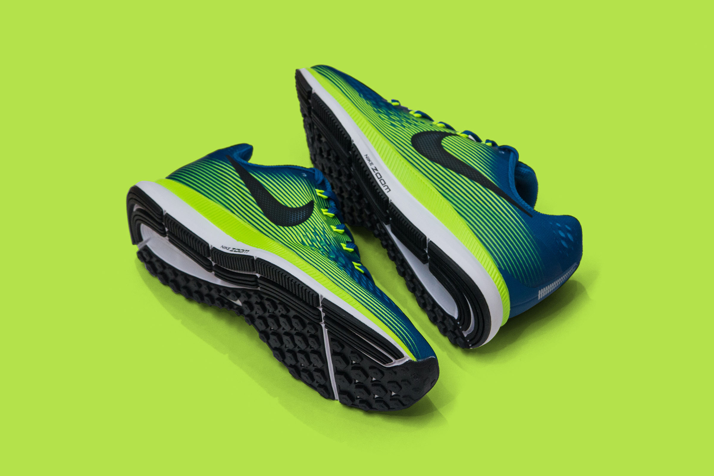 Neon green and blue Nike running shoes with black soles placed on a bright green background.